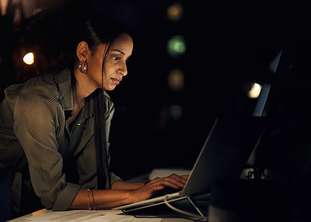code-sign-2 A woman working on a laptop in a dimly lit environment, focused on cybersecurity or data analysis.