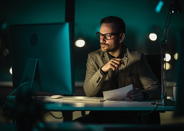 A man in a dark offic looking at monitor